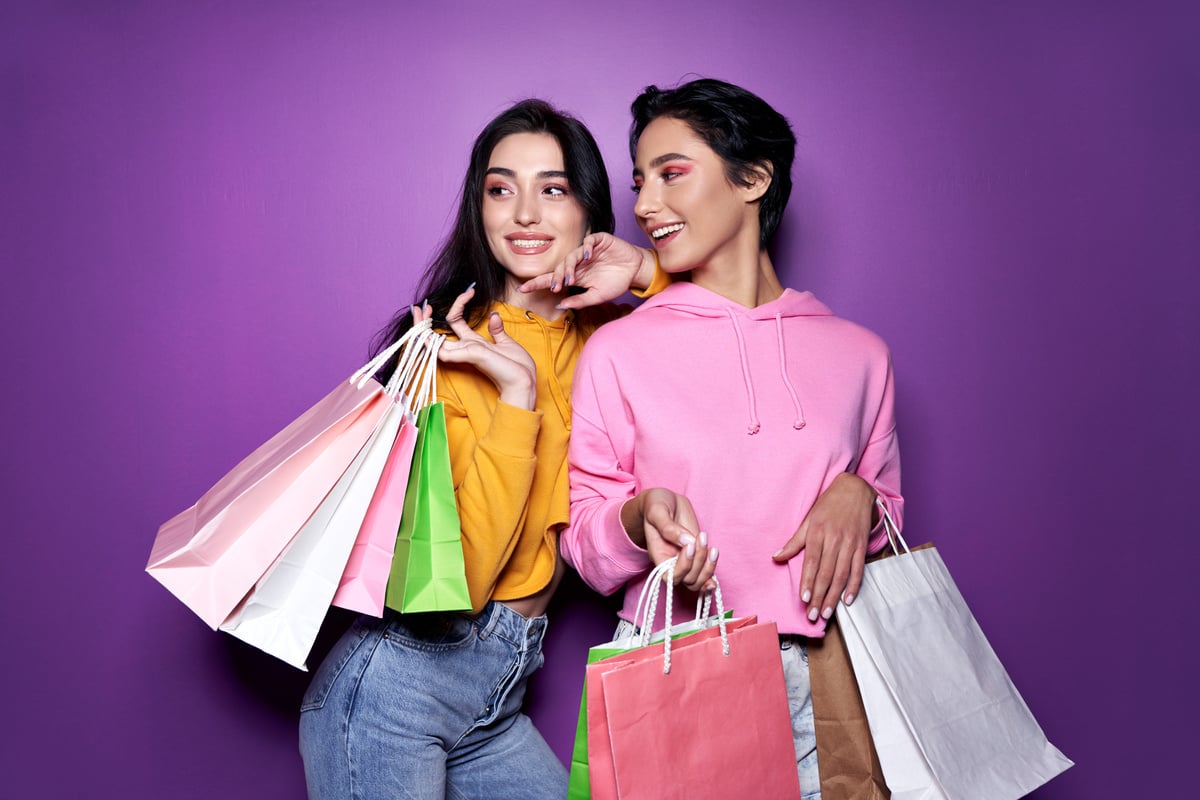 Two Female Friends with Shopping Bags on Purple Background